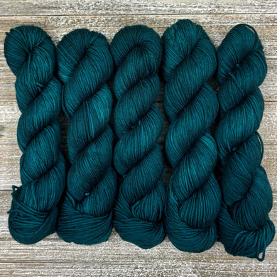 Five skeins of dark teal yarn on a wooden surface