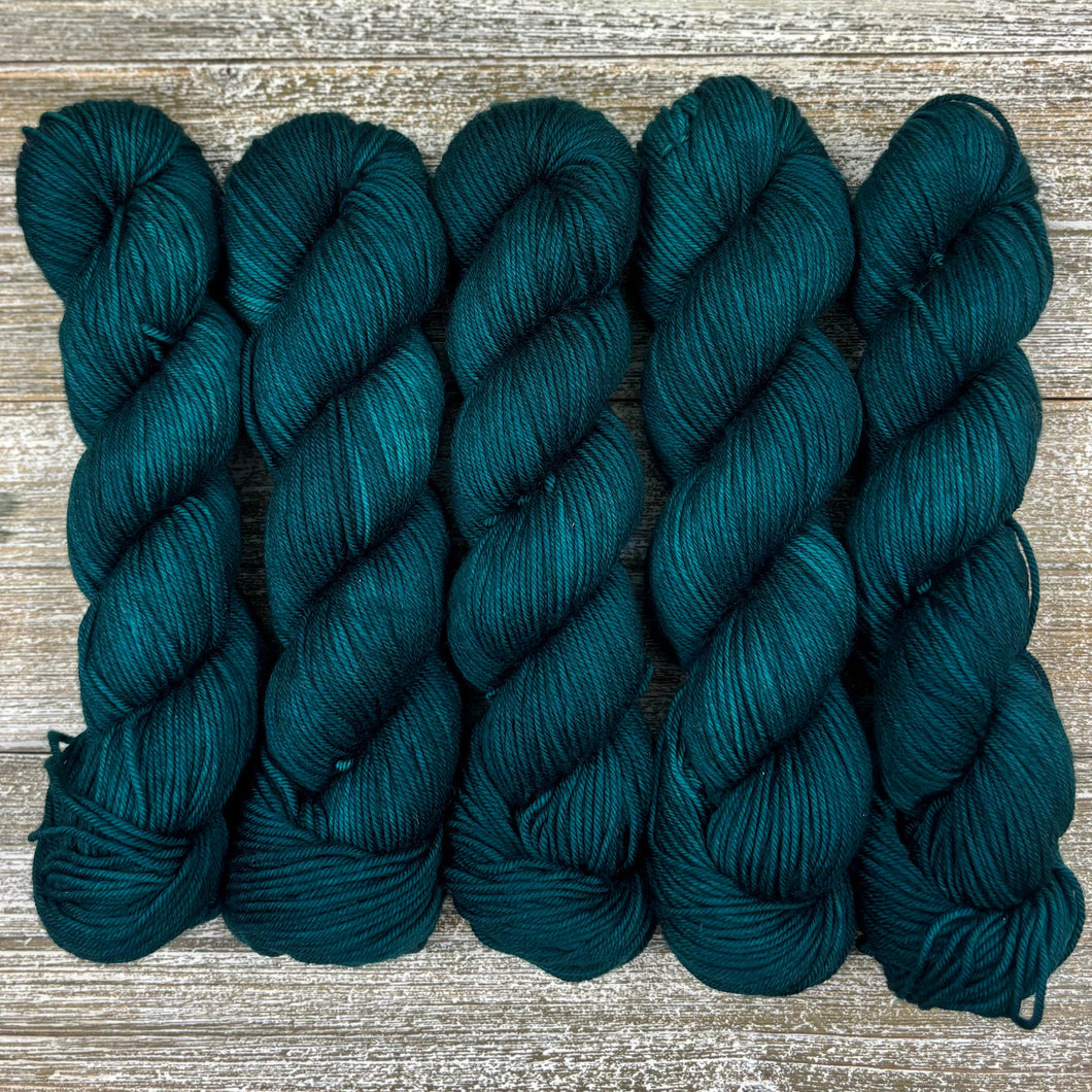 Five skeins of dark teal yarn on a wooden surface