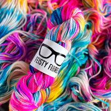 Load image into Gallery viewer, Florescent rainbow skein of yarn with a &#39;Feisty Fibres&#39; label amidst more yarn.
