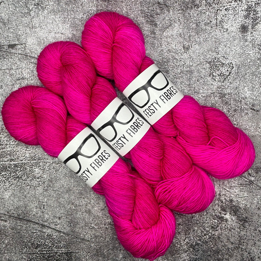 Three skeins of bright pink yarn with a label on a gray textured background