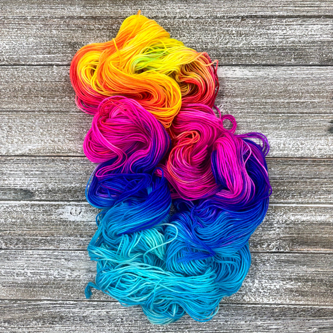  skein of colorful yarn in orange, pink, blue, and purple on a wooden surface.